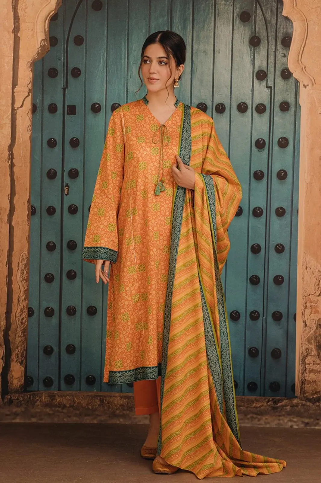 Model in a mustard printed lawn suit standing before an arched teal door