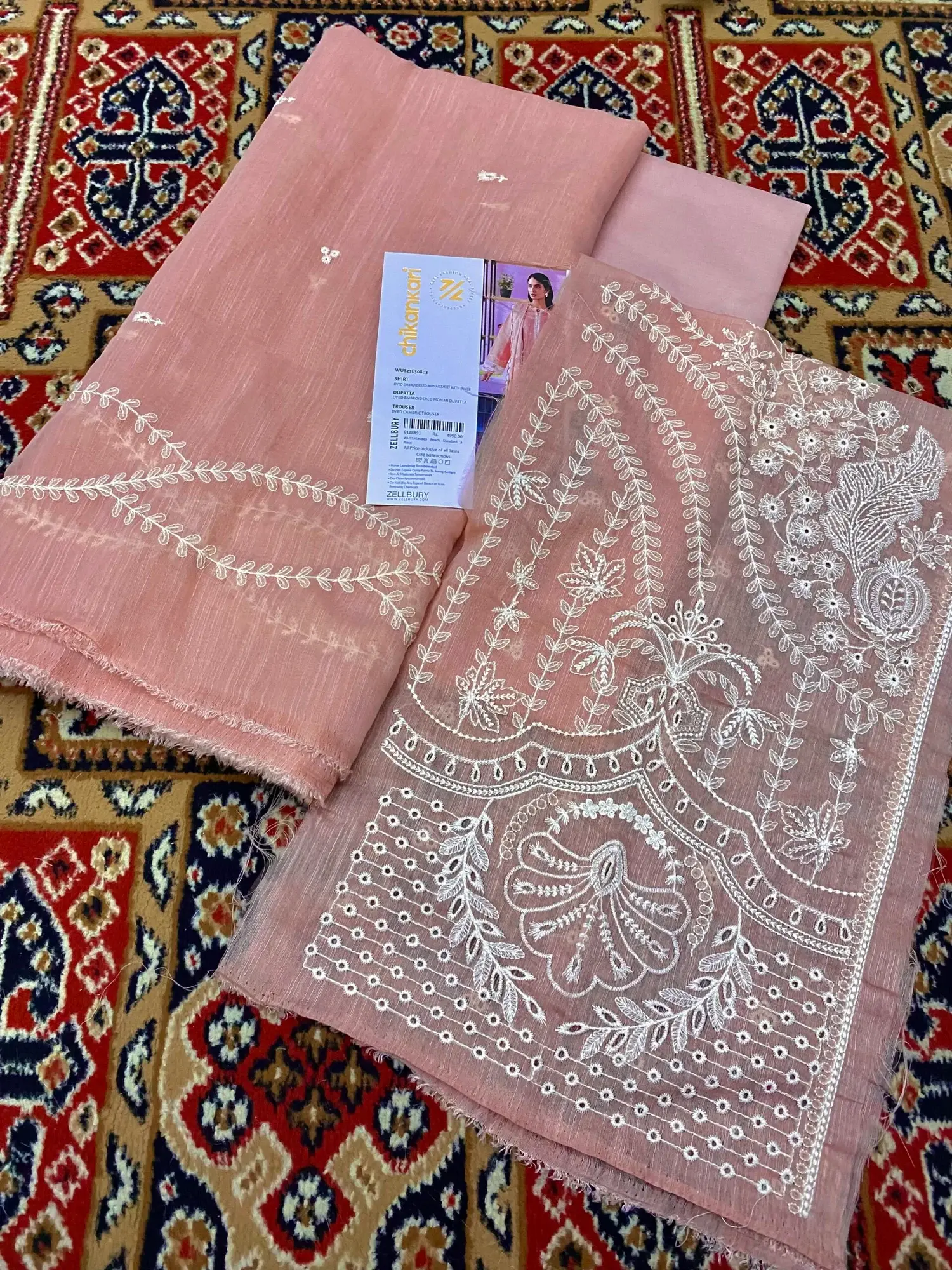 Folded blush pink embroidered lawn fabric laid on a patterned rug